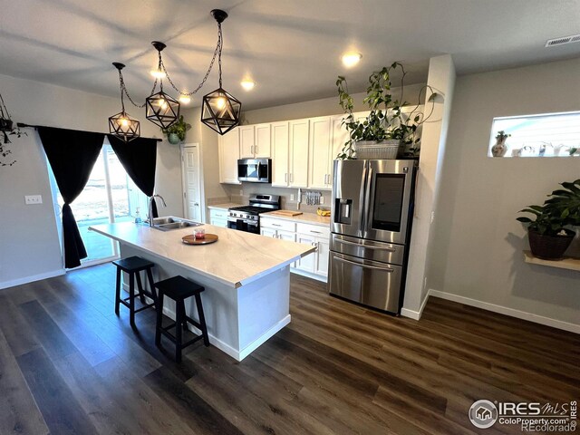 kitchen featuring decorative light fixtures, stainless steel appliances, a sink, light countertops, and a center island with sink