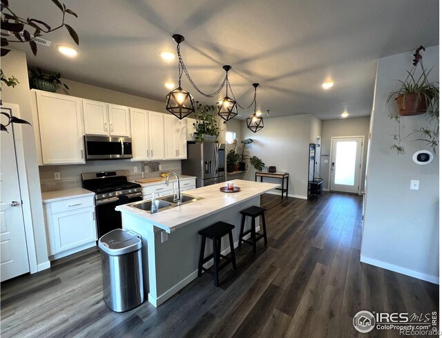 kitchen with a kitchen island with sink, stainless steel appliances, a sink, white cabinetry, and light countertops