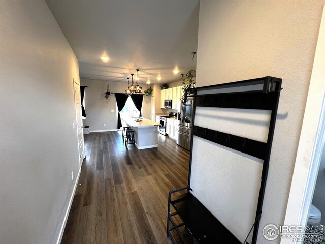 corridor featuring dark wood-style floors, baseboards, and a notable chandelier