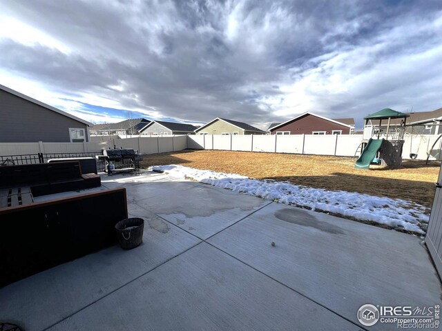 snow covered patio with a playground, a fenced backyard, and a residential view