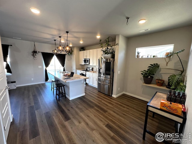 kitchen featuring a kitchen island with sink, stainless steel appliances, white cabinetry, a kitchen breakfast bar, and light countertops