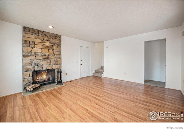 unfurnished living room featuring hardwood / wood-style floors, a stone fireplace, and a textured ceiling