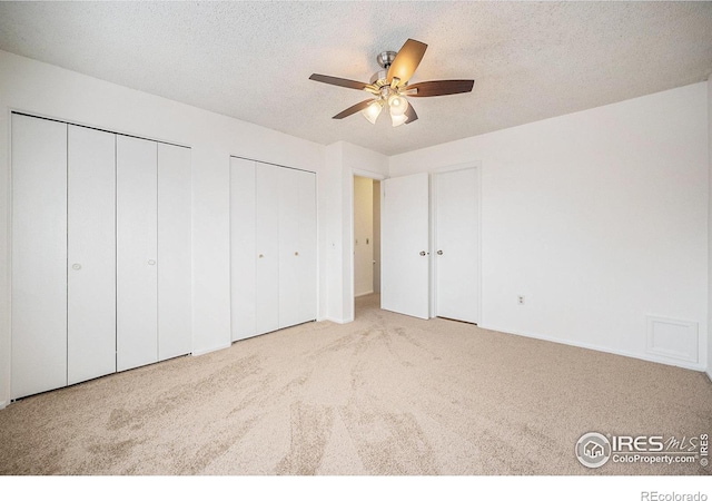 unfurnished bedroom featuring ceiling fan, a textured ceiling, light carpet, and multiple closets