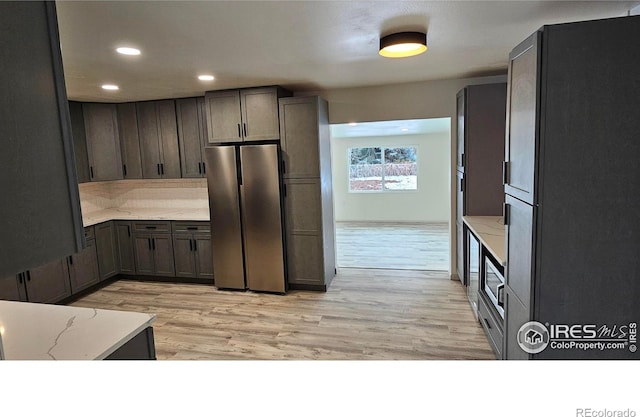 kitchen with light wood-type flooring, dark brown cabinets, stainless steel refrigerator, and refrigerator