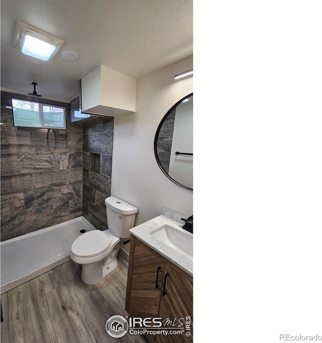 bathroom featuring a tile shower, vanity, wood-type flooring, and toilet