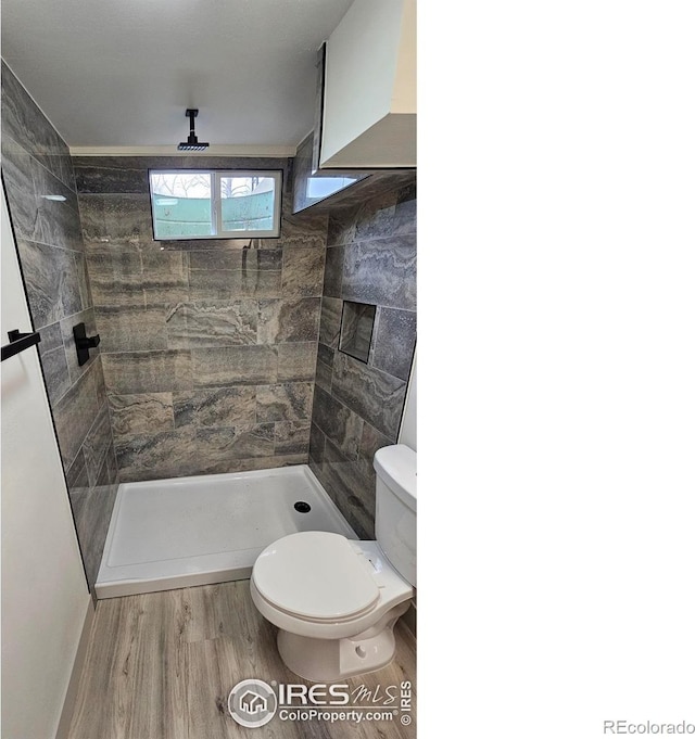 bathroom featuring a tile shower, wood-type flooring, and toilet