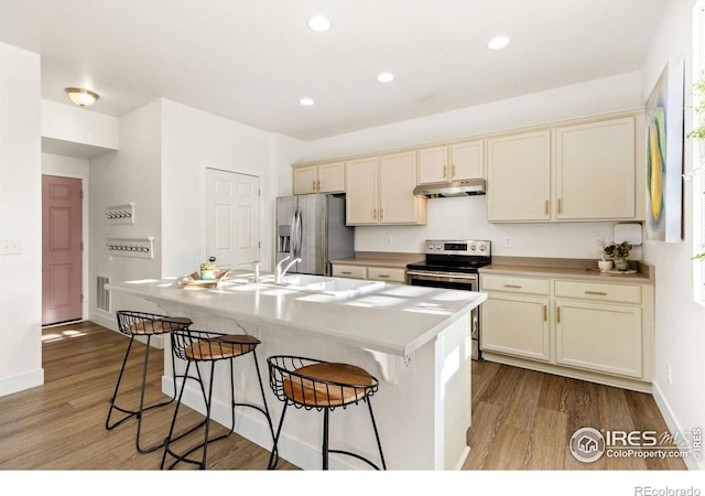 kitchen featuring a kitchen breakfast bar, cream cabinetry, a center island with sink, appliances with stainless steel finishes, and sink