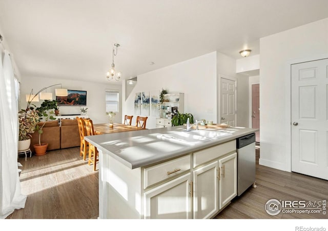 kitchen featuring dark wood-type flooring, stainless steel dishwasher, decorative light fixtures, a kitchen island with sink, and sink