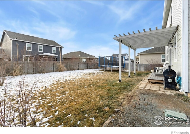 yard covered in snow featuring a wooden deck, a pergola, and a trampoline