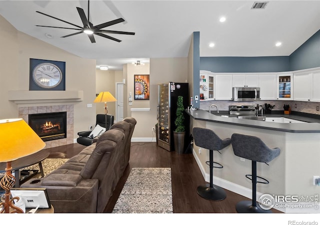 living room with a tile fireplace, dark hardwood / wood-style floors, sink, and ceiling fan