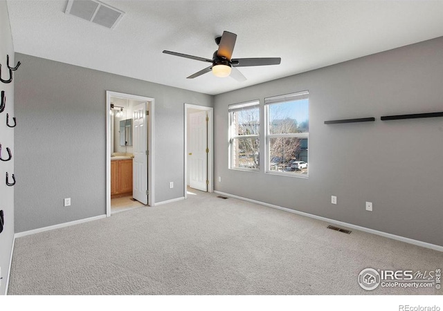 unfurnished bedroom featuring light colored carpet, ensuite bath, and ceiling fan