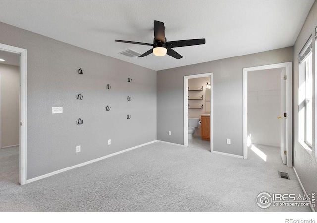 unfurnished bedroom featuring a walk in closet, light carpet, a closet, ceiling fan, and multiple windows