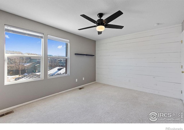 carpeted spare room with wood walls and ceiling fan