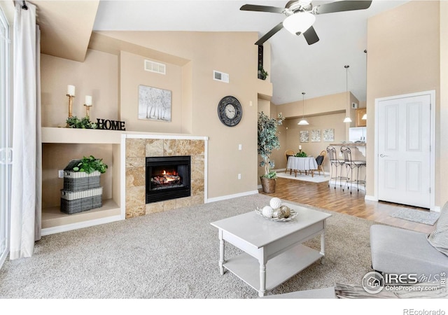 living room featuring carpet floors, high vaulted ceiling, ceiling fan, and a tiled fireplace