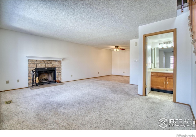 unfurnished living room featuring light carpet, a stone fireplace, sink, ceiling fan, and a textured ceiling