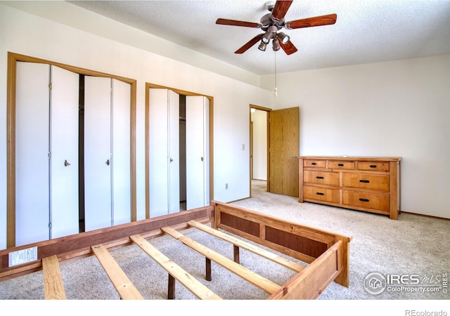 carpeted bedroom featuring a textured ceiling, ceiling fan, and multiple closets