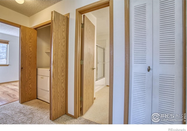 corridor featuring light colored carpet, a textured ceiling, and washer / clothes dryer