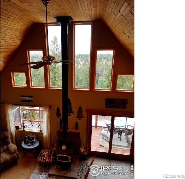 living room with a wood stove, ceiling fan, wood ceiling, and a wealth of natural light