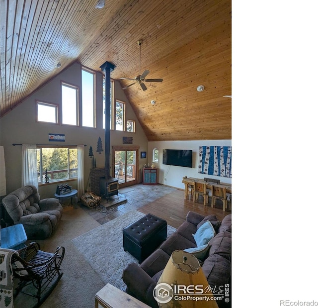 living room with wood ceiling, ceiling fan, a wood stove, and a high ceiling