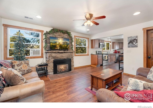 living room featuring wood-type flooring, a stone fireplace, ceiling fan, and cooling unit