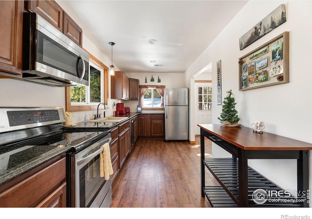 kitchen with pendant lighting, dark stone counters, sink, dark hardwood / wood-style floors, and appliances with stainless steel finishes