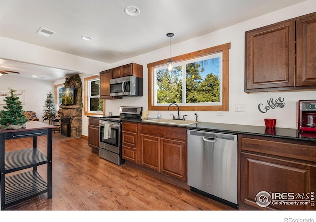 kitchen with dark stone counters, stainless steel appliances, sink, hardwood / wood-style flooring, and hanging light fixtures