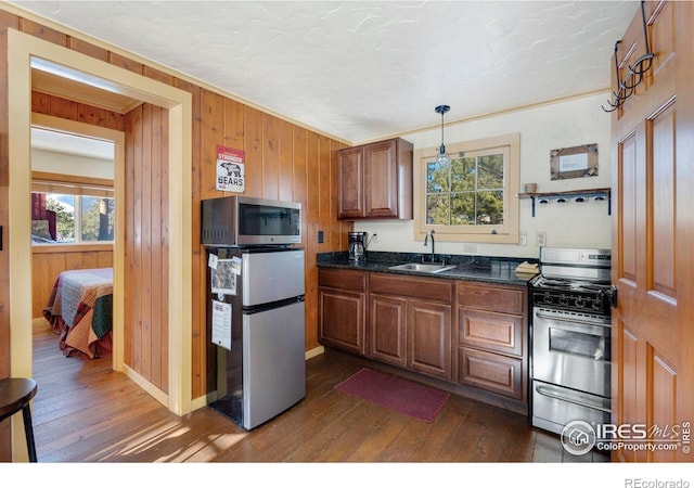 kitchen with pendant lighting, stainless steel appliances, wood walls, and sink