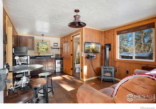 kitchen with sink, hanging light fixtures, dark wood-type flooring, wooden walls, and stainless steel stove