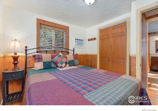 bedroom with a textured ceiling, wood walls, a closet, and a wall mounted air conditioner