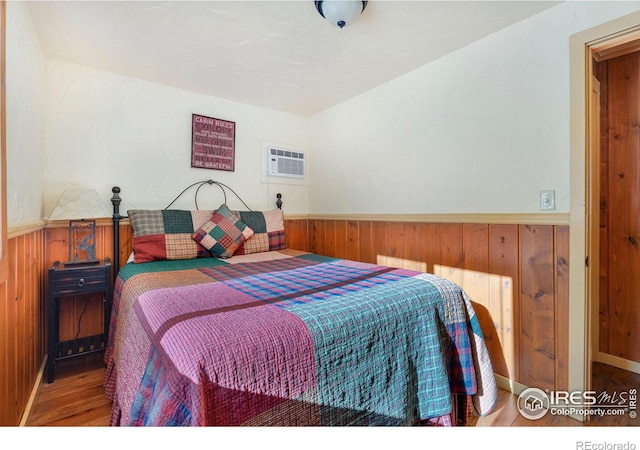 bedroom featuring a wall mounted air conditioner, hardwood / wood-style floors, and wooden walls