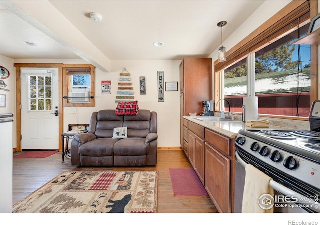 kitchen featuring sink, light stone counters, decorative light fixtures, light hardwood / wood-style floors, and white range oven