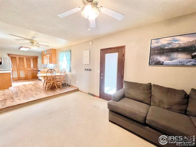 living room with light carpet, a textured ceiling, and ceiling fan