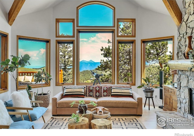 sunroom featuring a mountain view, lofted ceiling with beams, and a stone fireplace