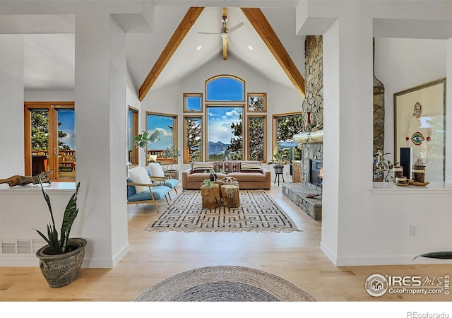 living room with ceiling fan, a fireplace, beamed ceiling, light hardwood / wood-style flooring, and high vaulted ceiling