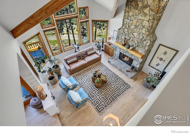 living room featuring high vaulted ceiling, beamed ceiling, a stone fireplace, and light hardwood / wood-style flooring