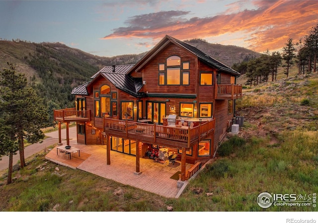 back house at dusk featuring central air condition unit, a deck with mountain view, and a patio