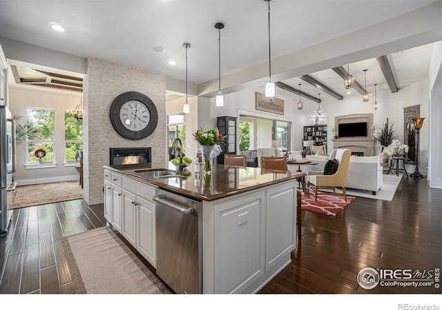 kitchen with stainless steel dishwasher, beamed ceiling, a fireplace, white cabinetry, and an island with sink