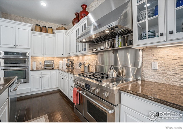 kitchen with white cabinetry, stainless steel appliances, dark stone counters, extractor fan, and decorative backsplash