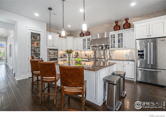 kitchen with white cabinets, hanging light fixtures, wall chimney range hood, and appliances with stainless steel finishes