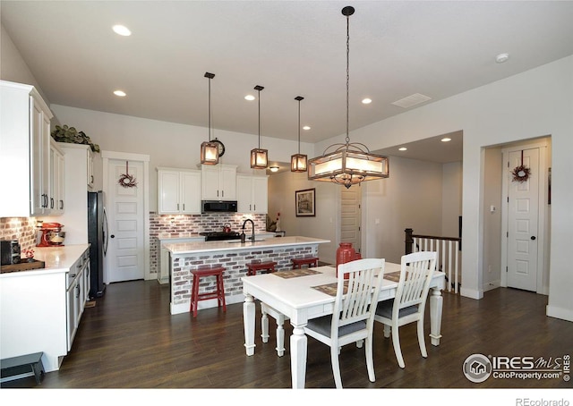 kitchen with a kitchen island with sink, backsplash, hanging light fixtures, appliances with stainless steel finishes, and white cabinetry