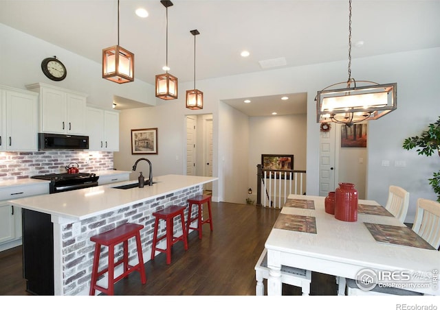 kitchen with hanging light fixtures, sink, black appliances, and a center island with sink