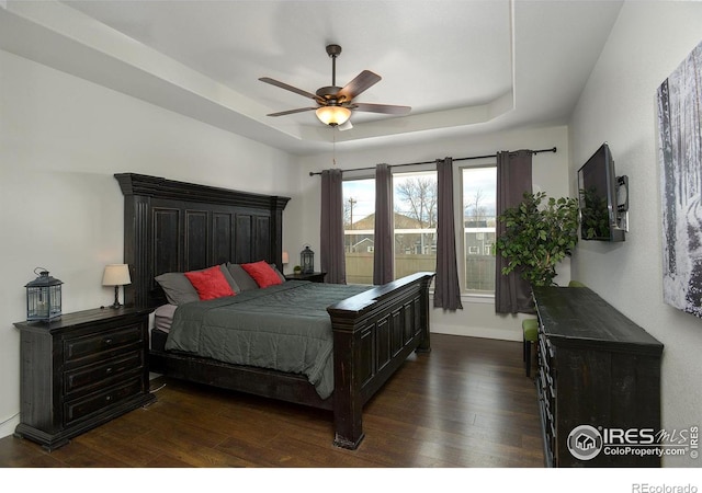 bedroom with a raised ceiling, ceiling fan, and dark wood-type flooring