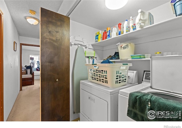 clothes washing area with washing machine and dryer, light carpet, and a textured ceiling