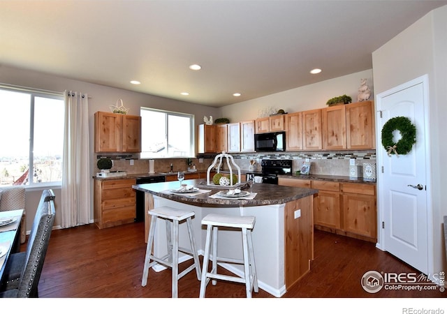 kitchen featuring backsplash, a breakfast bar, a healthy amount of sunlight, black appliances, and a center island