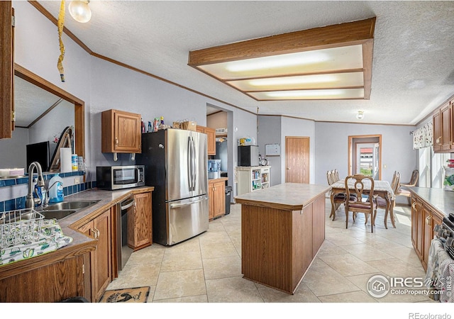 kitchen with sink, stainless steel appliances, a textured ceiling, a kitchen island, and ornamental molding