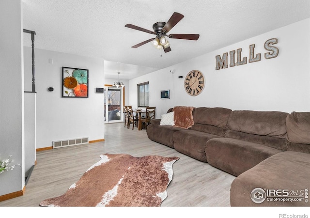 living room with a textured ceiling, ceiling fan with notable chandelier, and light hardwood / wood-style floors