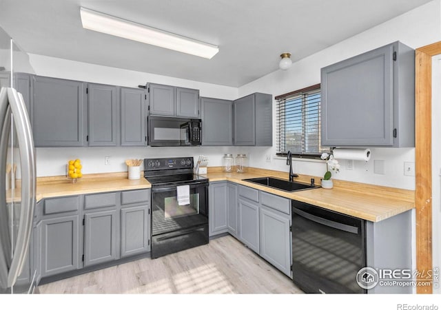 kitchen with gray cabinetry, sink, black appliances, and light hardwood / wood-style floors