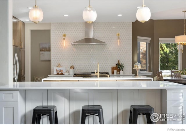 kitchen with decorative light fixtures, backsplash, stainless steel fridge with ice dispenser, and wall chimney exhaust hood