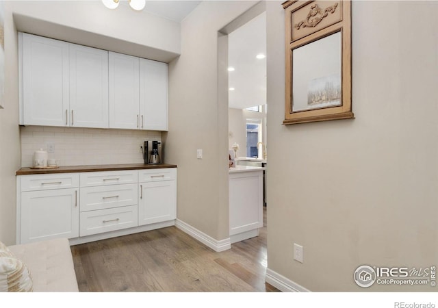 kitchen with white cabinets, butcher block countertops, light hardwood / wood-style floors, and backsplash