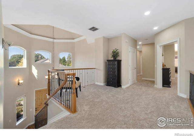 hall featuring light colored carpet, a raised ceiling, and ornamental molding